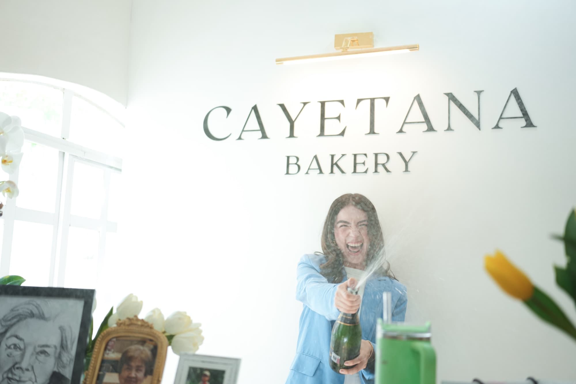 Cinthia Martínez descorchando champán bajo el letrero de Cayetana Bakery el día de la inauguración